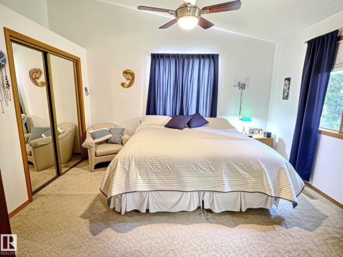 Vaulted ceiling bedroom featuring a ceiling fan with integrated lighting, mirrored closet doors, a window with blinds, and neutral carpeting - 171 Rhatigan Road, Edmonton, AB 