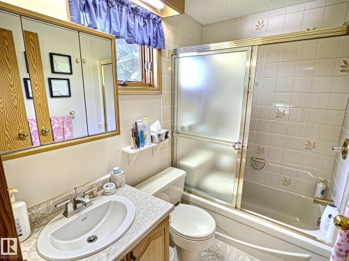Bathroom featuring a shower-tub combination with frosted glass sliding doors and full-height tile surround - 171 Rhatigan Road, Edmonton, AB 