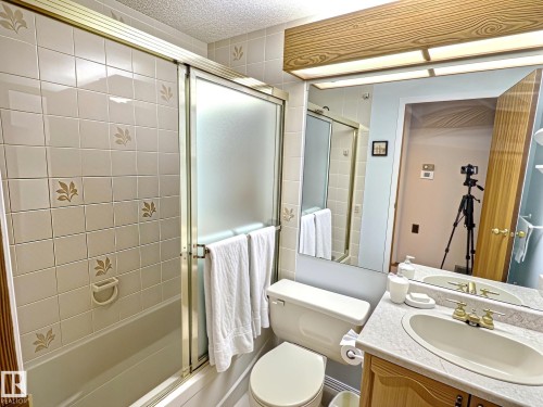 Bathroom featuring a bathtub with tiled surround, sliding glass shower doors, a built-in vanity with integrated sink, and an expansive wall mirror - 171 Rhatigan Road, Edmonton, AB 