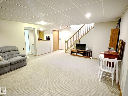 Spacious room featuring neutral carpet flooring, a drop ceiling with recessed lighting, and a wood staircase with balusters - 171 Rhatigan Road, Edmonton, AB 