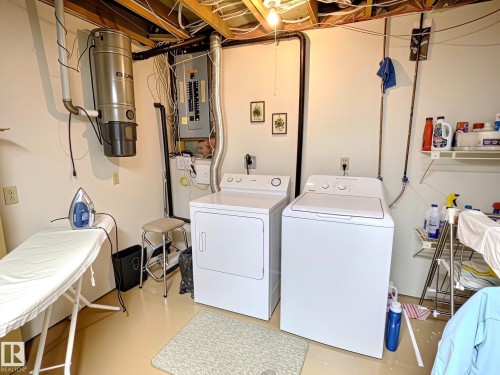 Dedicated laundry area featuring a washer and dryer, central vacuum system, exposed ceiling joists, and a visible electrical panel - 171 Rhatigan Road, Edmonton, AB 