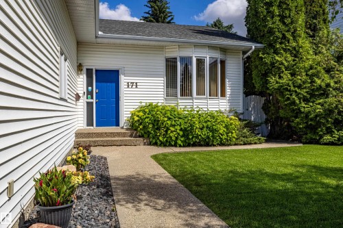 White siding exterior featuring a bright blue entry door, concrete walkway, bay window, and a green lawn - 171 Rhatigan Road, Edmonton, AB 