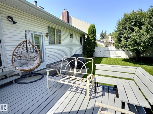Spacious outdoor deck with built-in bench seating, white vinyl siding, and a large grassy yard featuring mature trees - 171 Rhatigan Road, Edmonton, AB 