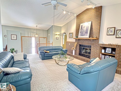 Spacious living area featuring a vaulted ceiling with a ceiling fan, a brick fireplace with a wood mantle, track lighting, and built-in shelving - 171 Rhatigan Road, Edmonton, AB 