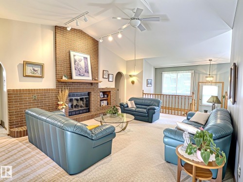 Living area featuring a brick fireplace with a wood mantle, vaulted ceilings, track lighting, and a ceiling fan - 171 Rhatigan Road, Edmonton, AB 