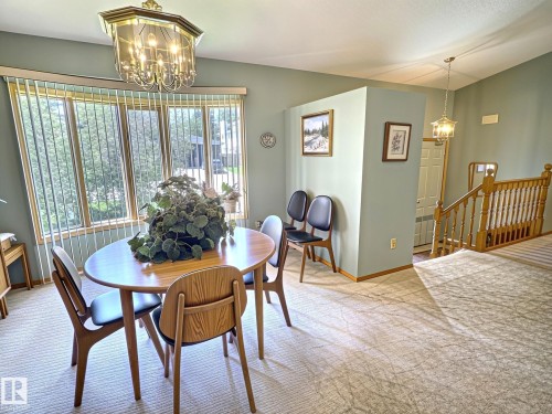 Dining area featuring a curved bay window with vertical blinds, a brass-finish chandelier, and light-toned patterned carpeting - 171 Rhatigan Road, Edmonton, AB 