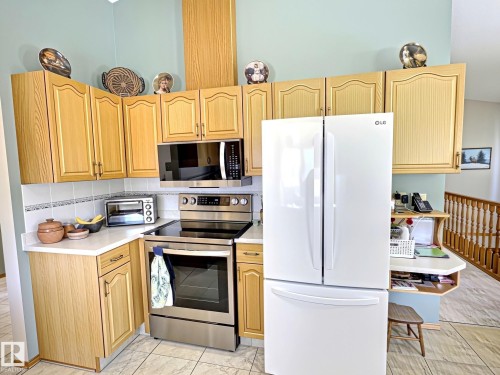 Kitchen featuring wood-finish cabinetry, white countertops, tile backsplash, and tile flooring - 171 Rhatigan Road, Edmonton, AB 