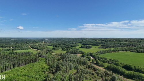 Expansive aerial perspective showcasing significant acreage with a mix of mature treed areas and open green spaces under a clear sky - 222A Range Rd, Rural Athabasca County, AB 