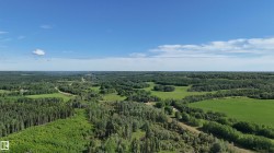 Expansive aerial perspective showcasing significant acreage with a mix of mature treed areas and open green spaces under a clear sky - 