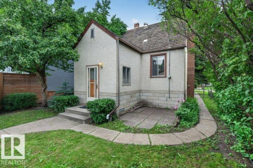 Stucco exterior with a peaked roofline, featuring a concrete front porch, an exterior light fixture, and a wooden privacy fence - 9026 92 Street Nw, Edmonton, AB - Outdoor