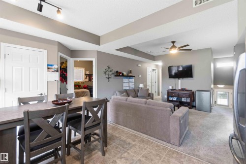 Open-concept interior featuring a breakfast bar, track lighting, ceiling fan, and mixed flooring with tile and carpet - 24 6520 2 Avenue, Edmonton, AB 