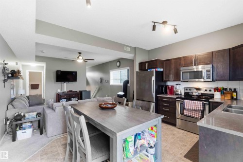 Open-concept kitchen and living area featuring wood-finish cabinetry, stainless steel appliances, a light-toned countertop, and a ceiling fan - 24 6520 2 Avenue, Edmonton, AB 