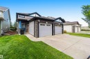 Contemporary residential exterior featuring stone veneer accents, light gray siding, a prominent teal entry door, a two-car attached garage, and a concrete driveway - 24 6520 2 Avenue, Edmonton, AB 
