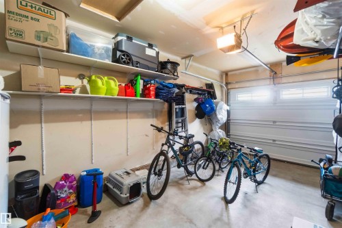 Attached garage featuring a white overhead door with upper window panels, overhead lighting, and built-in wall shelving - 24 6520 2 Avenue, Edmonton, AB 