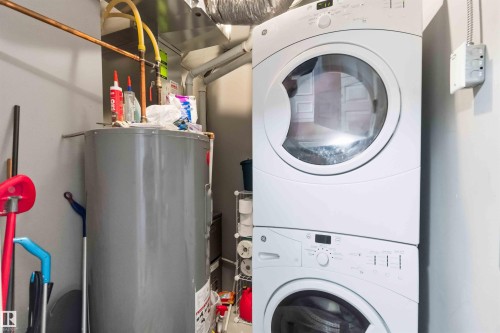 Dedicated utility space featuring a stacked washer and dryer unit, a water heater, visible copper piping, and exposed ductwork - 24 6520 2 Avenue, Edmonton, AB 