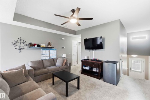 Spacious living area featuring neutral carpeting, a ceiling fan with integrated lighting, and recessed ceiling details - 24 6520 2 Avenue, Edmonton, AB 