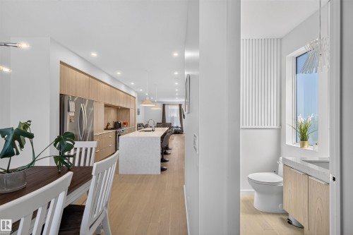 Open-concept living area with wood-finish flooring extending into the kitchen, featuring light wood-tone cabinetry and stainless steel appliances - 8551 81 Avenue, Edmonton, AB 