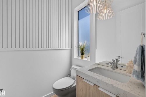 Powder room featuring a vertical slat accent wall, a rectangular window, a light wood-finish vanity with an integrated sink, and an overhead decorative light fixture - 8551 81 Avenue, Edmonton, AB 
