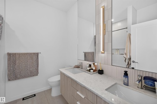 Contemporary bathroom featuring a light wood-finish double vanity with quartz countertops, integrated sinks, and wall-mounted mirrors - 8551 81 Avenue, Edmonton, AB 
