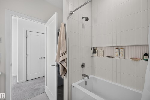 Modern white bathtub and shower combination featuring vertical subway tile surround - 8551 81 Avenue, Edmonton, AB 