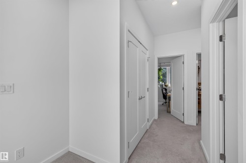 Hallway featuring light gray carpeting, white trim, recessed lighting, and multiple paneled doors with contemporary hardware - 8551 81 Avenue, Edmonton, AB 