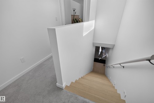 Hardwood stairs with a light wood finish and a white handrail, complemented by bright white walls and light gray carpeting - 8551 81 Avenue, Edmonton, AB 