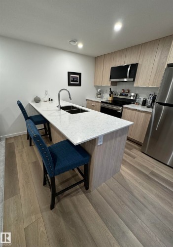 Modern kitchen featuring a central island with a double basin sink and a light-toned countertop - 8551 81 Avenue, Edmonton, AB 