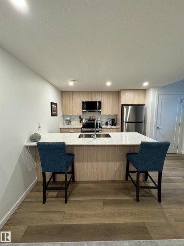 Open-concept kitchen featuring light wood-finish cabinetry, stainless steel appliances, and wood-finish flooring - 8551 81 Avenue, Edmonton, AB 