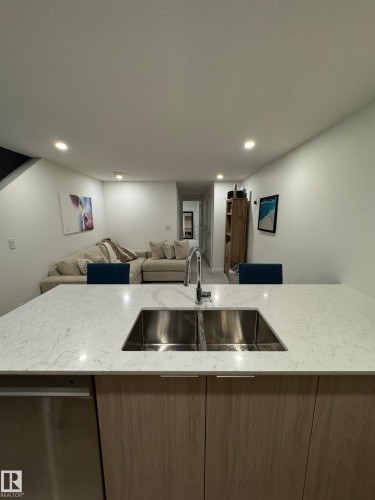 Kitchen island featuring a double basin stainless steel sink, a chrome gooseneck faucet, and light-toned wood-finish cabinetry - 8551 81 Avenue, Edmonton, AB 