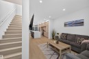Open-concept living space with light wood-finish flooring, recessed lighting, a modern staircase with a white handrail, and a kitchen featuring light wood cabinetry and a white island with a built-in sink - 8551 81 Avenue, Edmonton, AB 