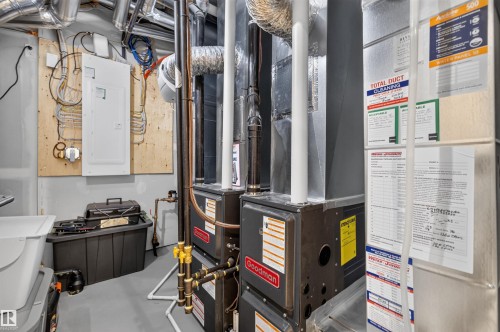 Utility room featuring two Goodman furnaces, exposed ductwork, and a wall-mounted electrical panel - 8551 81 Avenue, Edmonton, AB 