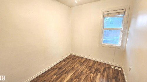 Bright room featuring wood-finish flooring, light-toned walls, and a single window with white trim - 9359 92 Street, Edmonton, AB 