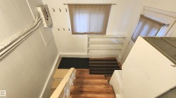 Wood-finish stairs leading to a landing with built-in shelving and two windows - 