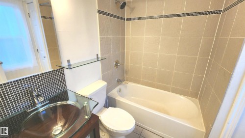 Bathroom featuring a glass vessel sink, dark wood-finish vanity, and black mosaic tile backsplash - 9359 92 Street, Edmonton, AB 