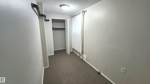Room featuring wall-to-wall carpeting, neutral wall paint, and a built-in closet with shelving and hanging rod - 9359 92 Street, Edmonton, AB 