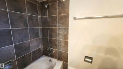 Bathtub with dark-toned wall tiling, coordinating shower head, and chrome fixtures - 