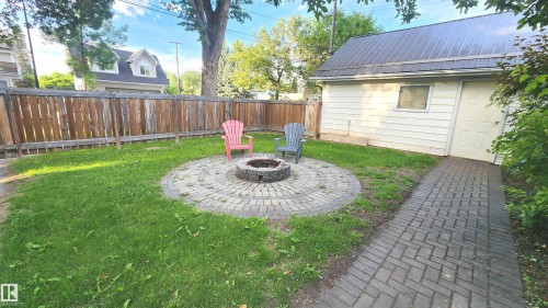 Backyard featuring a circular paver fire pit area, manicured lawn, and a full wood privacy fence - 9359 92 Street, Edmonton, AB 