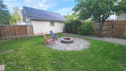 Spacious backyard featuring a circular paver patio with a built-in stone fire pit, a detached garage with a dark metal roof, and a privacy fence - 9359 92 Street, Edmonton, AB 