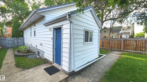 White siding exterior with a vibrant blue entrance door, multiple windows, and a paved walkway - 9359 92 Street, Edmonton, AB 