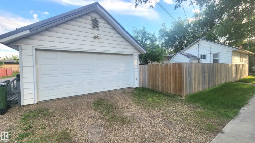 Detached garage with panel-style door, gravel driveway, and wood privacy fencing - 9359 92 Street, Edmonton, AB 
