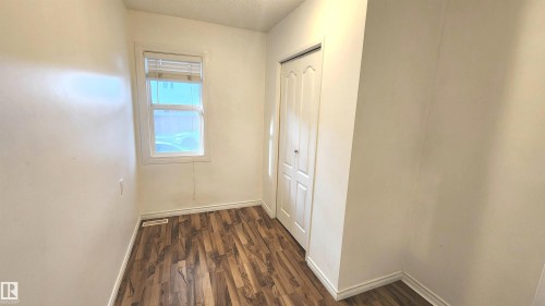 Room featuring wood-finish flooring, white baseboards, a single window with horizontal blinds, and a white bi-fold closet door - 9359 92 Street, Edmonton, AB 