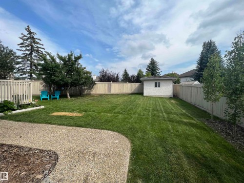 Expansive backyard featuring a large lawn, mature trees, wood fencing, and a white storage shed with a window - 1417 115A Street, Edmonton, AB - Outdoor With Backyard