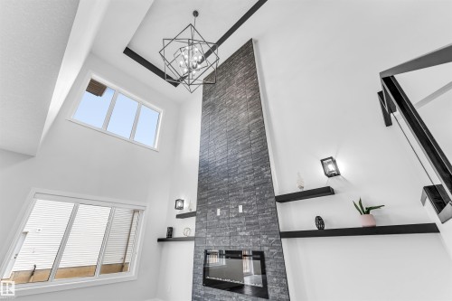 Soaring ceilings featuring a geometric chandelier, a floor-to-ceiling stone-look fireplace with an integrated linear electric insert, and multiple windows - 11 Southbridge Crt, Calmar, AB 