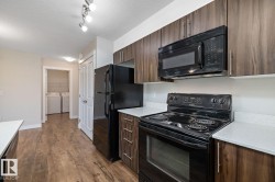 Kitchen featuring wood-finish flooring, dark wood-finish cabinetry, light countertops, black appliances, and track lighting - 