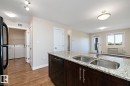 Kitchen island featuring a double basin stainless steel sink with a gooseneck faucet, light granite-style countertop, and dark wood-finish cabinetry - 4615 199 Street, Edmonton, AB 