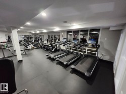 Fitness center featuring durable black flooring, recessed lighting, expansive mirrored wall, large windows, and white walls - 