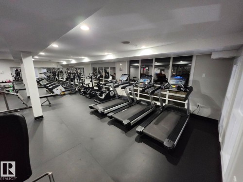 Fitness center featuring durable black flooring, recessed lighting, expansive mirrored wall, large windows, and white walls - 4615 199 Street, Edmonton, AB 