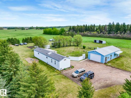 Expansive property featuring a white residence with a dark roof, a light blue outbuilding with a white garage door, and a gravel driveway - 53133 Rge Road 223, Rural Strathcona County, AB - Outdoor With View