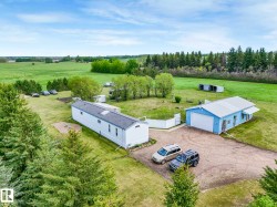 Expansive property featuring a white residence with a dark roof, a light blue outbuilding with a white garage door, and a gravel driveway - 
