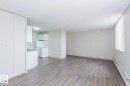 Open-concept living area featuring wood-finish flooring, white walls, and a large window with vertical blinds - 8510 111 Street, Edmonton, AB 